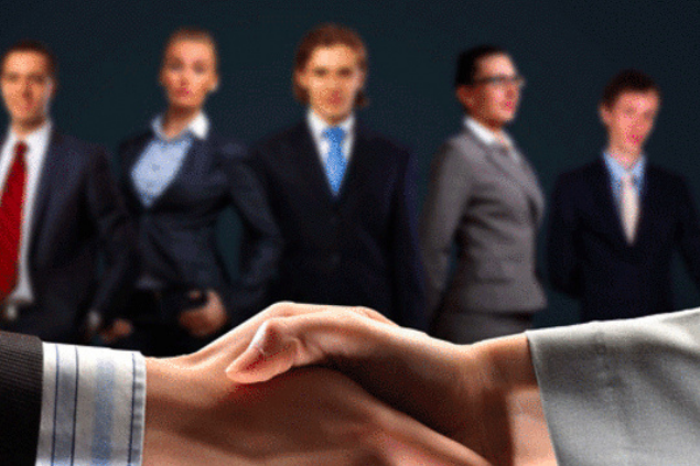 Two businessmen shaking hands in front of a corporate backdrop